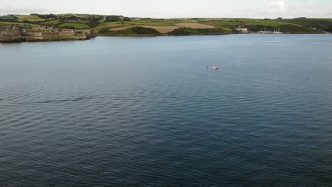 Drone-footage-of-a-SUP-boarder-and-boat-in-the-middle-of-a-very-wide-blue-river-with-distant-Charles-Fort-and-green-hills