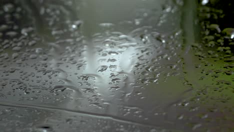 Car-taillights-drive-down-a-road,-seen-through-a-rain-streaked-windshield