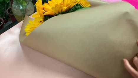 Ein-örtlicher-Florist-Verpackt-Einen-Strauß-Frisch-Geschnittener-Sonnenblumen-In-Braunes-Metzgerpapier