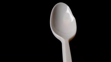 Flame-melts-hole-from-behind-in-plastic-spoon-against-black-background