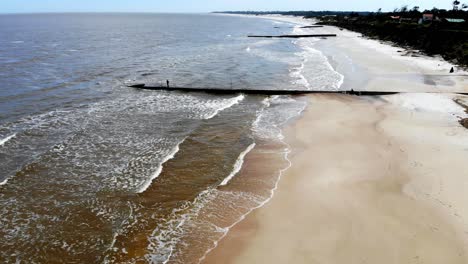 Luftaufnahme-Des-Strandes-Mit-Wellenbrechern-Und-Menschen-Beim-Angeln-An-Einem-Sonnigen-Tag