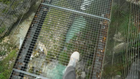POV,-man-in-trainers-walking-on-iron-bridge-over-carved-mountain-river