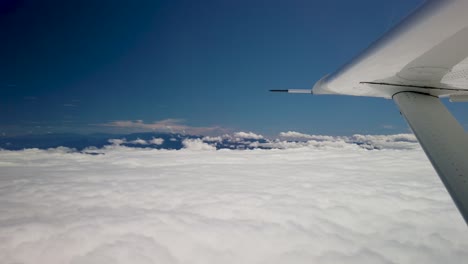 Flying-above-thick-white-clouds-in-small-airplane,-view-of-wing