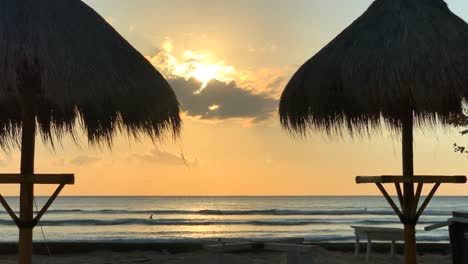 Puesta-De-Sol-Bali-Indonesia,-2-Sombrillas-Tiki-En-La-Playa
