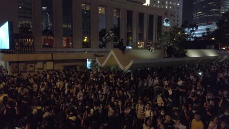 Demonstrant-Sitzt-Auf-Einem-Erhöhten-Felsvorsprung-Und-Schwenkt-Die-Flagge-„Befreit-Hongkong“,-Während-Sich-Eine-Menschenmenge-Darunter-Befindet,-Hongkong