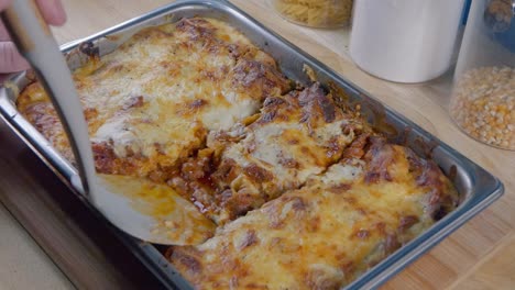 Medium-Shot-of-Serving-a-Portion-of-Lasagne-from-the-Baking-Tray-on-the-Kitchen-Counter