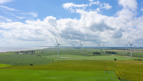 Lufthyperlapse-Von-Windkraftanlagen-Und-Wolken,-Während-Der-Wind-Wellen-Auf-Den-Feldern-Schlägt