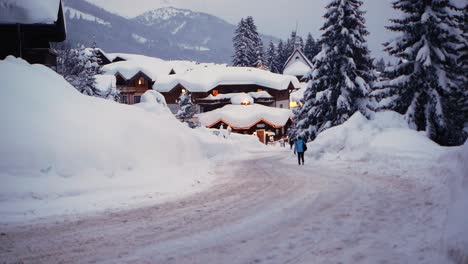 Menschen,-Die-Während-Der-Blauen-Stunde-Mit-Lichtern-über-Eine-Schneebedeckte-Straße-In-Einem-Dorf-Laufen