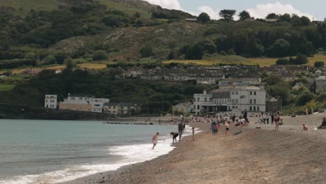 Adults-and-kids-playing-on-the-beach-on-a-sunny-day,-with-houses-and-hills-in-the-background