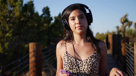Beautiful-young-hispanic-woman-listening-to-music-on-her-headphones-and-smartphone-while-smiling-and-being-happy-SLOW-MOTION