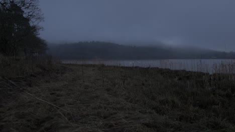 Island-shore-line-dusk-tilt-reveal-fog-covered-distant-forest