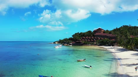 Friedliche-Türkisfarbene-Lagune,-Die-Weißen-Sandstrand-Unter-Blauem-Himmel-Mit-Weißen-Wolken-Auf-Einer-Tropischen-Insel-Mit-Resorts-In-Thailand-Umspült