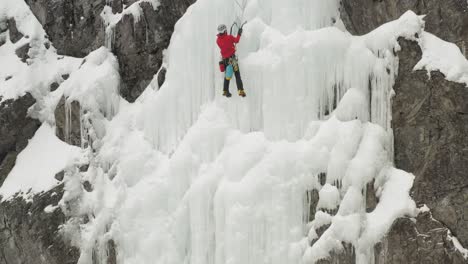 Climber-climbs-frozen-ice-sheet-cascade-with-axes-aerial-4K