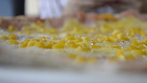 Detailed-view-of-pizza-with-ham-and-sweetcorn-with-a-girl-sitting-behind-and-playing-with-her-phone,-PANNING