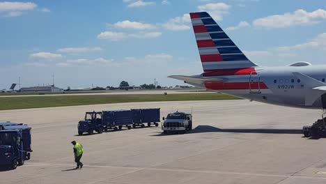 Marshaller-walking-to-luggage-cart,-planes-taking-off-in-background,-Dallas-Texas-airport