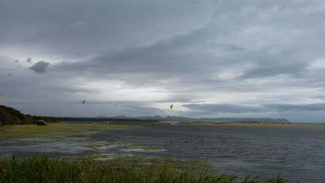 Kitesurfers-on-lagoon,-moody-skies,-long-shot