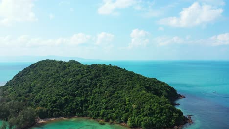 Isolated-tropical-island-with-trees-forest-and-rocky-shoreline-in-the-middle-of-colorful-lagoon-with-clear-turquoise-water-and-coral-reefs,-ko-tae-nai,-Thailand