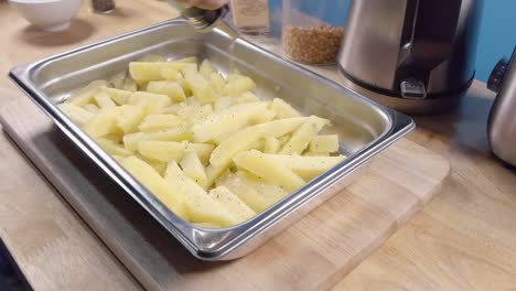 Slow-Motion-Slider-Shot-of-Drizzling-Oil-on-Homemade-Oven-Fries-in-a-Metal-Baking-Tray-Prior-to-Cooking-in-the-Kitchen