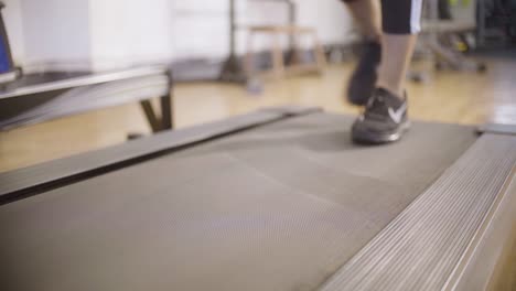 Asian-girl-comes-and-steps-on-treadmill-with-sports-shoes-on-at-gym