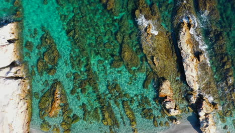 Aerial-top-down-view-moving-right-slowly,-mediterranean-sea-crystal-clear-water-and-beautiful-long-rocks