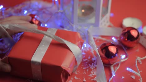 Lösen-Eines-Silbernen-Schleifenbandes-Auf-Einem-Weihnachtsgeschenk-Mit-Rotem-Papier-Mit-Rotem-Hintergrund-Und-Kugeln