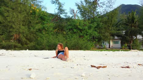Schönes-Blondes-Mädchen,-Das-Auf-Dem-Weißen-Sand-Eines-Exotischen-Strandes-Liegt-Und-Sich-Unter-Wunderschönem-Sonnenlicht-Auf-Einer-Tropischen-Insel-Mit-üppiger-Vegetation-Entspannt