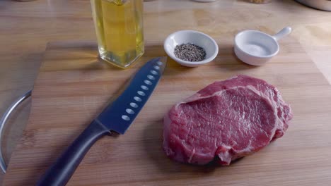 Zeitlupen-Slider-Aufnahme-Eines-Rohen-Ribeye-Steaks-Auf-Einem-Holzschneidebrett-Vor-Dem-Kochen