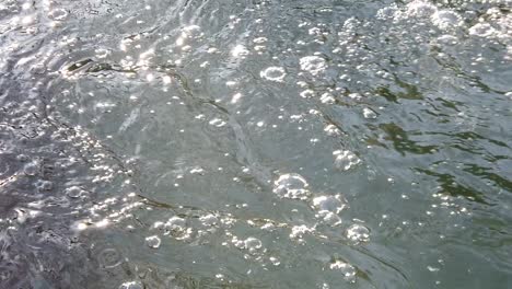 Slow-motion-of-the-water-between-rocks-and-ice,-forming-bubble-and-ripple-of-the-surface