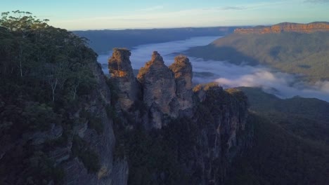 The-Three-Sisters-rocks-formation-at-Blue-Mountains-with-view-of-clouds-covering-the-rainforest-trees,-Sydney-Australia