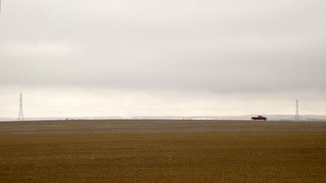 Pickup-truck-driving-left-to-right-on-rural-road-in-arid-farm-landscape-during-winter,-static-long-shot