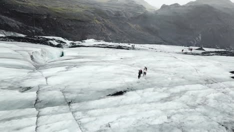 Ice-Snow-and-Group-of-Hikers-on-Icelandic-Solheimajokull-Glacier,-Cinematic-Aerial,-Climate-Change-and-Global-Warming-Concept
