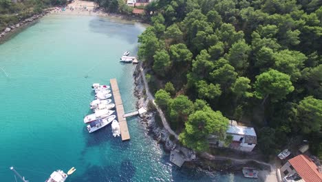 Descending-aerial-view-from-drone-approaching-the-blue-water-of-the-Adriatic-with-boats-at-a-wooden-dock-of-a-marina-on-Hvar-island,-Croatia