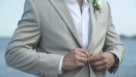 Groom-buttoning-suit-jacket-closed-by-coast