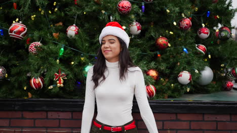 Eine-Wunderschöne-Hispanische-Frau,-Die-Mit-Einer-Weihnachtsmütze-Tanzt-Und-Lacht-Und-Die-Fröhliche-Weihnachtszeit-Mit-Einem-Weihnachtsbaum-Feiert