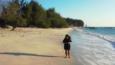Young-tourist-woman-walking-barefoot-alone-on-white-sand-of-exotic-beach,-enjoying-beautiful-seascape-and-fresh-air-of-tropic,-Indonesia