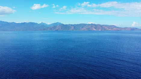 Panoramic-blue-sea-space-bordered-by-high-mountains-of-islands-under-bright-sky-with-frozen-white-clouds-in-Indonesia