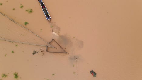Fischer-Verlassen-Ein-Boot-In-Der-Nähe-Von-Fischnetzfallen-Mit-Pfeilspitze,-Die-Braune,-Schlammige,-überflutete-Wasserstraßen-Des-Mekong-Deltas-Aufwirbeln