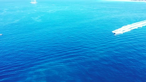 Boat-sailing-across-blue-azure-sea-surface,-tracing-calm-clear-water-by-white-waves,-copy-space-with-sea-texture