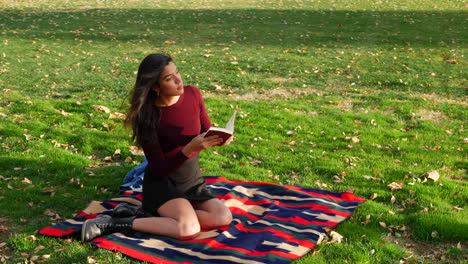 A-young-woman-student-reading-a-story-book-and-relaxing-between-school-classes-in-the-university-park