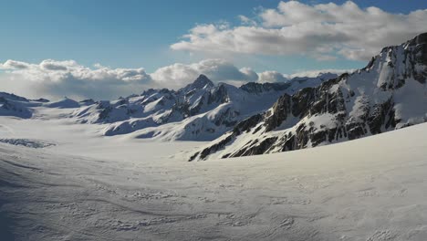 Stunning-4K-drone-shot-flying-over-snowy-saddle-to-reveal-huge-mountains-on-far-side