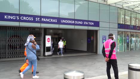 Man-wearing-protective-equipment-and-a-bright-pink-vest-directs-members-of-the-public-outside-Kings-Cross-Station,-London,-UK