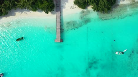 Malediven,-Wunderschöner,-Ruhiger-Weißer-Sandstrand-Mit-Holzdeck,-Tropischen-Bäumen-Und-Booten,-Die-Im-Ruhigen-Türkisfarbenen-Wasser-Schwimmen