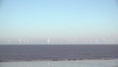 A-family-with-a-push-chair-and-dogs-walk-along-the-beach-near-Ingoldmells-in-front-of-the-huge-Lincs-wind-farm,-that-lies-eight-kilometres-offshore-in-the-North-Sea-off-the-East-Coast-of-England