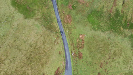 Aerial-top-down-view,-following-a-black-car-driving-on-a-rural-road,-bright-day