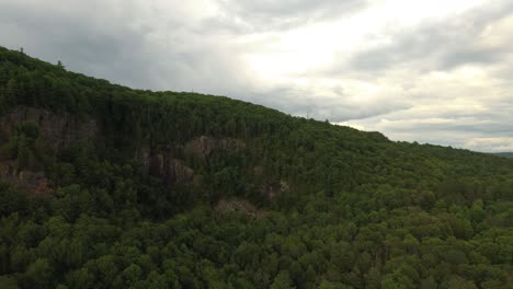 Sideway-rising-drone-shot-of-side-of-mountain-with-rocky-walls-and-clouds