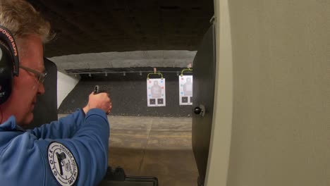 Man-shooting-with-a-pistol-at-paper-target-at-an-indoor-shooting-range-with-him-wearing-ear-protection
