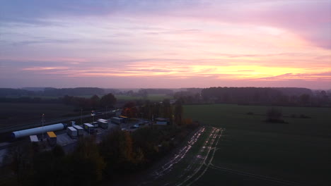 Slow-aerial-forward-showing-golden-hour-beside-truck-parking-area-and-motorway,germany