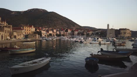 View-of-Komiza,-its-many-docked-boats-in-the-cove,-and-the-castle-at-dusk-with-gentle-waves
