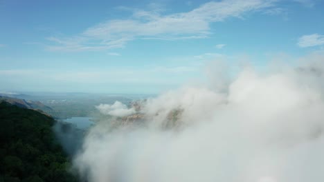 Forward-drone-shot-through-fog-clouds,-over-forest-mountains-towards-a-distant-lake-of-Western-Ghats