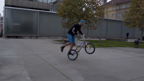 Guy-riding-a-BMX-bike-in-a-skatepark,-performing-the-Peg-Manual-trick
